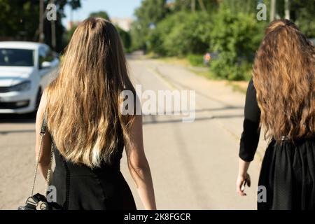Deux filles en robes noires marchent sur la route. Les filles reviennent de funérailles. Vêtements noirs. Marche dans les robes de soirée pendant la journée. Banque D'Images