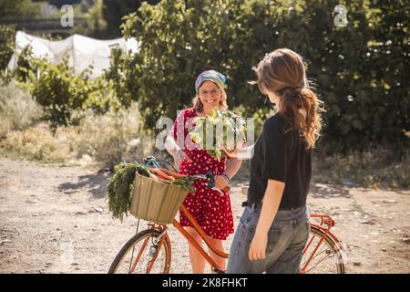 Agriculteur donnant de la laitue à la femme avec un vélo dans la ferme Banque D'Images