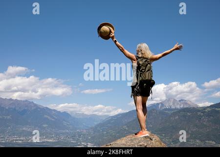 Femme sénior sans souci avec des bras levés debout sur le rocher en face des montagnes Banque D'Images