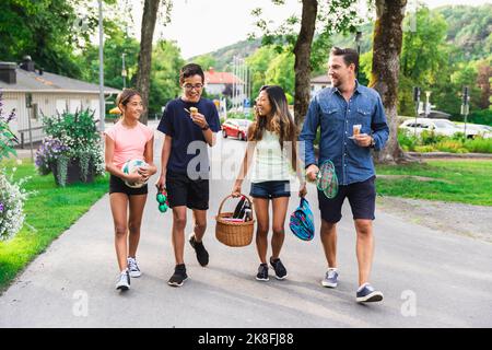 Bonne famille multiraciale avec des fournitures de pique-nique sur la route Banque D'Images