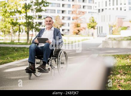 Homme senior souriant tenant un Tablet PC assis sur un fauteuil roulant Banque D'Images