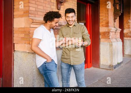 Des amis heureux regardant sur un téléphone portable près du mur Banque D'Images
