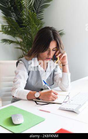 Un jeune avocat parle au téléphone intelligent et écrit des notes au bureau Banque D'Images