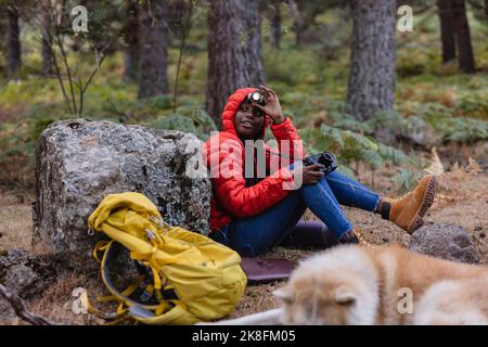 Femme portant une lampe de poche assise avec un appareil photo en forêt Banque D'Images