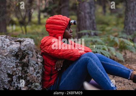 Jeune femme portant une lampe de poche assise dans la forêt Banque D'Images