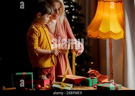 Mère coupe ruban enseignant fils à emballer des cadeaux à la maison Banque D'Images