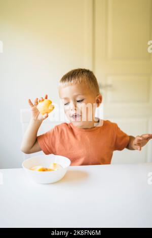 Mignon garçon ayant une pomme sur la table à manger à la maison Banque D'Images