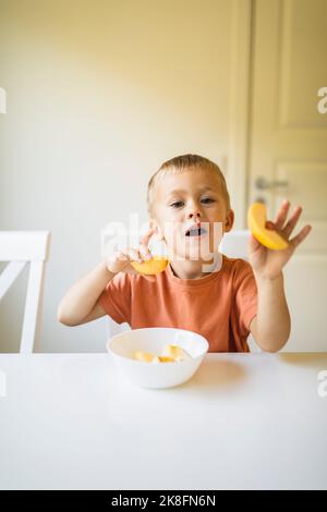 Garçon tenant des tranches de pomme à la table de salle à manger à la maison Banque D'Images