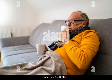 Homme toussant assis sur un canapé dans la salle de séjour Banque D'Images