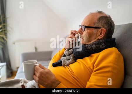 Homme âgé utilisant un vaporisateur nasal assis sur un canapé à la maison Banque D'Images