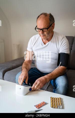 Homme mesurant la tension artérielle à travers l'appareil assis sur le canapé à la maison Banque D'Images