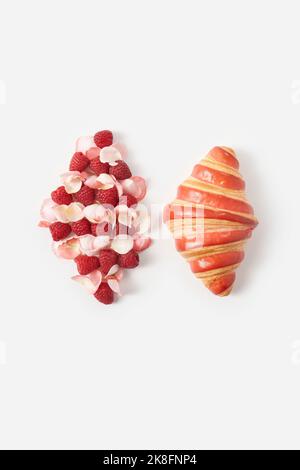 Croissant frais par framboises et pétales de rose de forme similaire sur fond blanc Banque D'Images