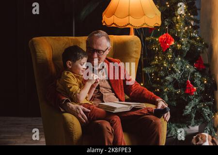 Petit-fils assis sur le livre de lecture de grand-père à la maison Banque D'Images