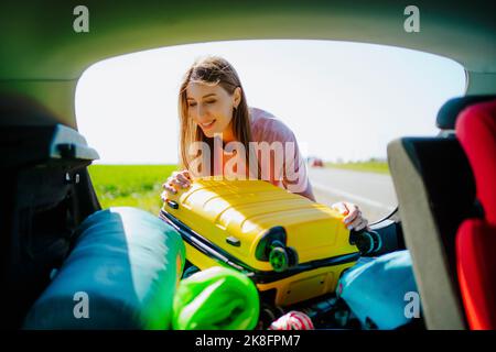 Femme souriante chargeant des bagages dans le coffre de voiture Banque D'Images