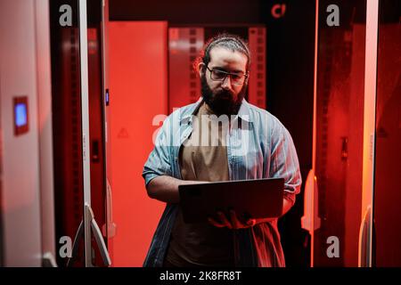 Expert INFORMATIQUE travaillant sur un ordinateur portable dans une salle de serveurs avec une lumière rouge au néon Banque D'Images