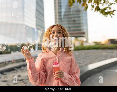 Bonne jeune femme jouant avec des bulles dans la rue Banque D'Images