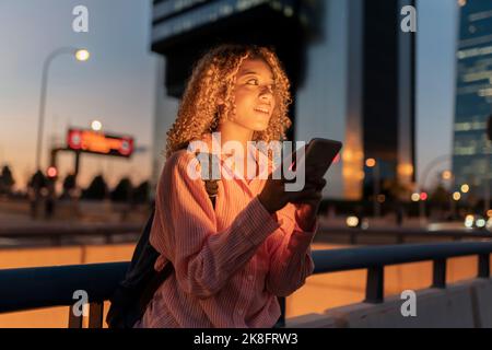 Femme aux cheveux mauriquement avec téléphone mobile contemplant la nuit Banque D'Images