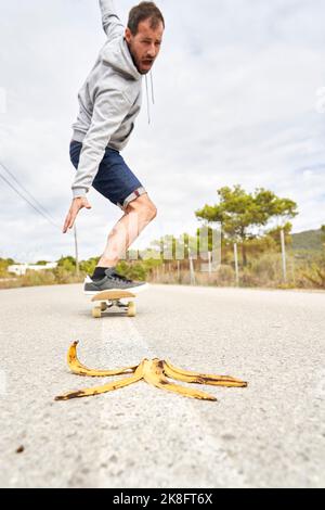 Homme terrifié skate par pelure de banane sur la route Banque D'Images