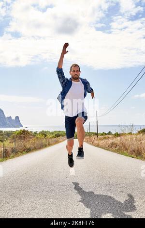 Homme à la main levé sautant sur la route Banque D'Images