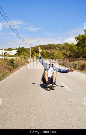 Homme levé à la main et faisant du skateboard sur la route Banque D'Images