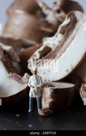 Champignons de châtaigne tranchés sur une planche à découper en ardoise, avec un chef miniature en uniforme Banque D'Images