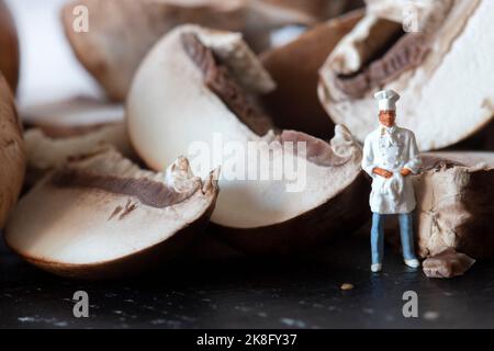 Champignons de châtaigne tranchés sur une planche à découper en ardoise, avec un chef miniature en uniforme Banque D'Images