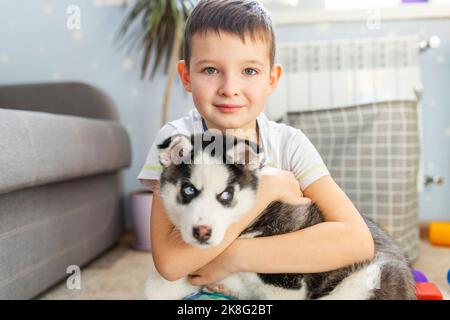 Un enfant mignon qui embrasse un chiot de chien husky sibérien assis sur le sol Banque D'Images