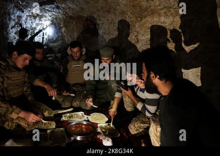 Idlib, Syrie. 23rd octobre 2022. Les combattants de l'opposition syrienne armée, connue sous le nom de Front de libération nationale (NFL), se nourrissent ensemble dans un tunnel souterrain sur les lignes de front face aux forces du régime syrien, dans la campagne d'Idlib. Credit: Aras Alkharboutli/dpa/Alamy Live News Banque D'Images