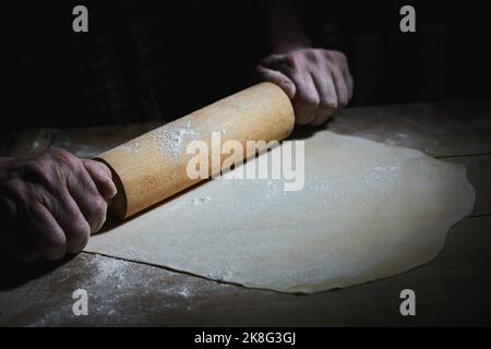 Crop anonyme chef cuisinier roulant de pâte sur table en bois recouvert de farine dans la boulangerie Banque D'Images