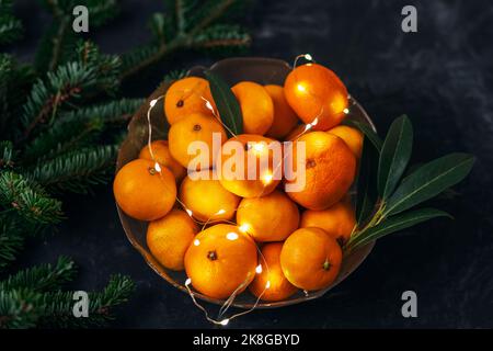 Bol avec mandarines fraîches, lumières de Noël et branches de sapin. Vue de dessus Banque D'Images