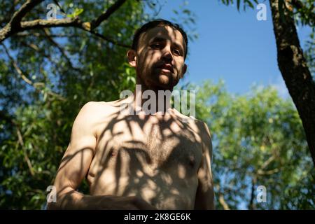 Guy à l'ombre des plantes sans vêtements. Homme en été. Banque D'Images