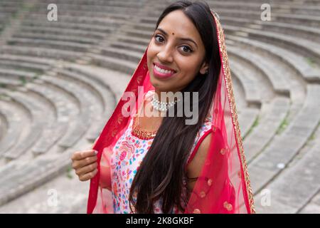 Vue d'en haut de côté de la jeune femme indienne heureuse dans l'ensemble traditionnel sari souriant et regardant l'appareil photo près des marches de pierre antiques Banque D'Images