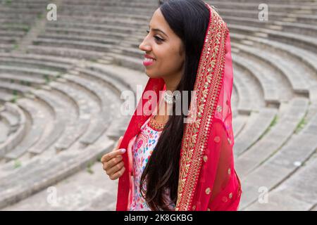 Vue d'en haut de côté de la jeune femme indienne heureuse dans l'ensemble traditionnel sari souriant et regardant loin près des escaliers de pierre anciens Banque D'Images