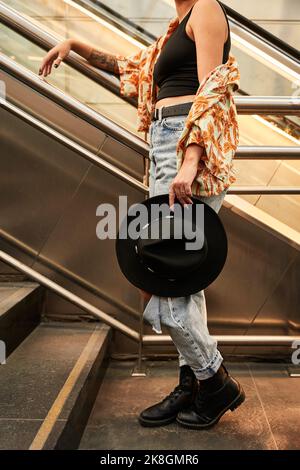 Femme méconnue dans des vêtements décontractés avec chapeau élégant debout près des escaliers dans le passage souterrain en journée à Madrid, Espagne Banque D'Images