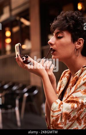 Jeune femme regardant dans le miroir et se maillant rouge à lèvres noir tout en appliquant le maquillage sur la rue de Madrid, Espagne Banque D'Images