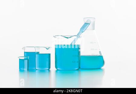 Collection de flacons de laboratoire en verre de différentes tailles et formes remplis de liquide bleu vif placé sur une surface blanche en studio Banque D'Images