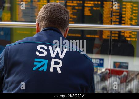 SWR, logo des chemins de fer du sud-ouest sur la veste de l'employé devant l'affichage de l'heure de la gare de waterloo, londres, royaume-uni Banque D'Images