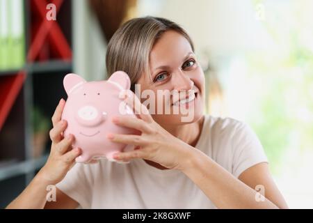 Femme souriante tenant une banque de porc rose entre les mains Banque D'Images