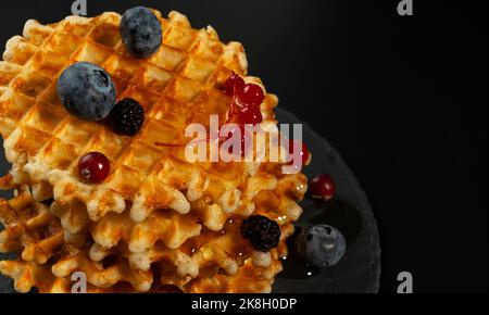 Gaufres belges fraîches croustillantes, myrtilles fraîches, mûres et raisins de Corinthe rouges, servies avec du miel frais en gros plan Banque D'Images