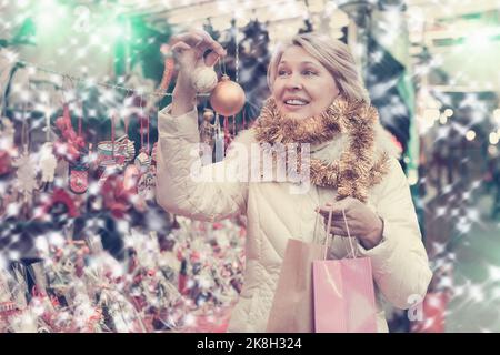 Bonne femme mûre en guirlande avec des jouets de Noël à la foire Banque D'Images