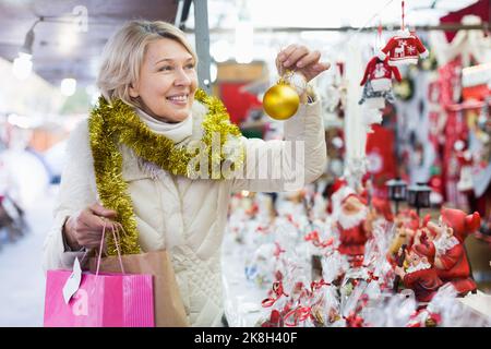 Bonne femme mûre en guirlande avec des jouets de Noël à la foire Banque D'Images