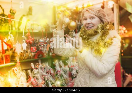 Bonne femme mûre en guirlande avec des jouets de Noël à la foire Banque D'Images