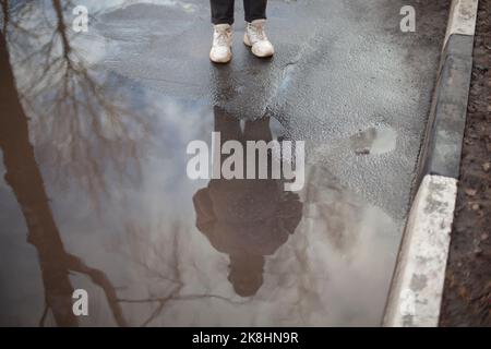 Réflexion de la personne dans la flaque. Bas de porte extérieur. La personne se tient sur une route humide. Pieds sur asphalte. Banque D'Images