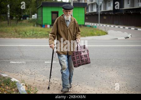 Le grand-père traverse la route. Grand-père avec bâton. Homme avec une barbe grise dans la rue. A pris sa retraite en Russie. Pauvre homme dans des vêtements pauvres. Vie sociale. Banque D'Images