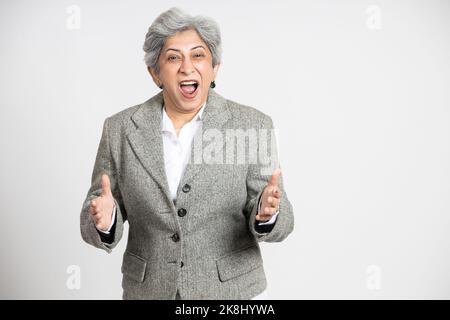 Une femme d'affaires indienne en colère, patron en costume debout contre fond blanc de studio, une femme d'affaires asiatique à cheveux gris 60s hurlant. Banque D'Images