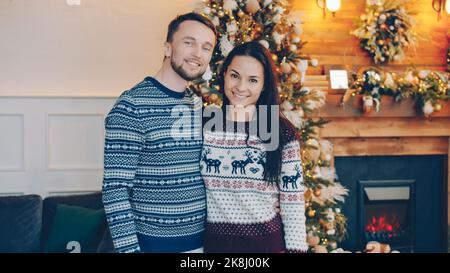 Portrait d'un couple heureux homme et femme debout ensemble le soir de Noël souriant et regardant l'appareil photo, les gens portent des chandails chauds. Banque D'Images