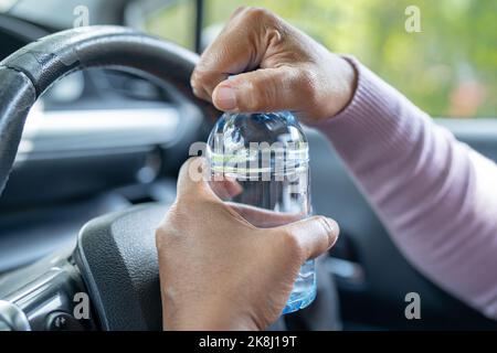 Femme asiatique chauffeur tenant une bouteille pour boire de l'eau tout en conduisant une voiture.Une bouteille d'eau chaude en plastique peut provoquer un incendie. Banque D'Images