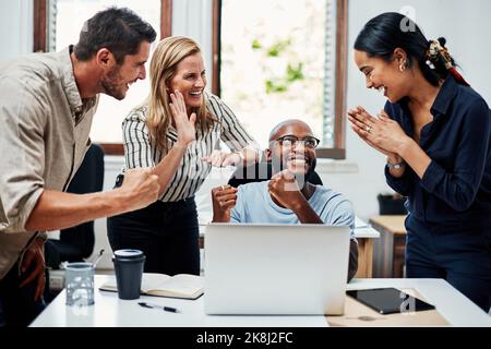 C'est incroyable. Un groupe de collègues qui applaudissent tout en se rassemblait autour d'un ordinateur portable au bureau. Banque D'Images