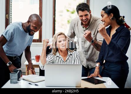 Oui. Un groupe de collègues d'affaires applaudissent tout en se réunissant autour d'un ordinateur portable au bureau. Banque D'Images