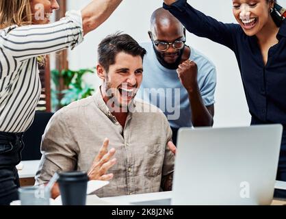 C'est l'affaire la plus importante de l'histoire de l'entreprise. Un groupe de collègues se réjouissent tout en se réunissant autour d'un ordinateur portable au bureau. Banque D'Images